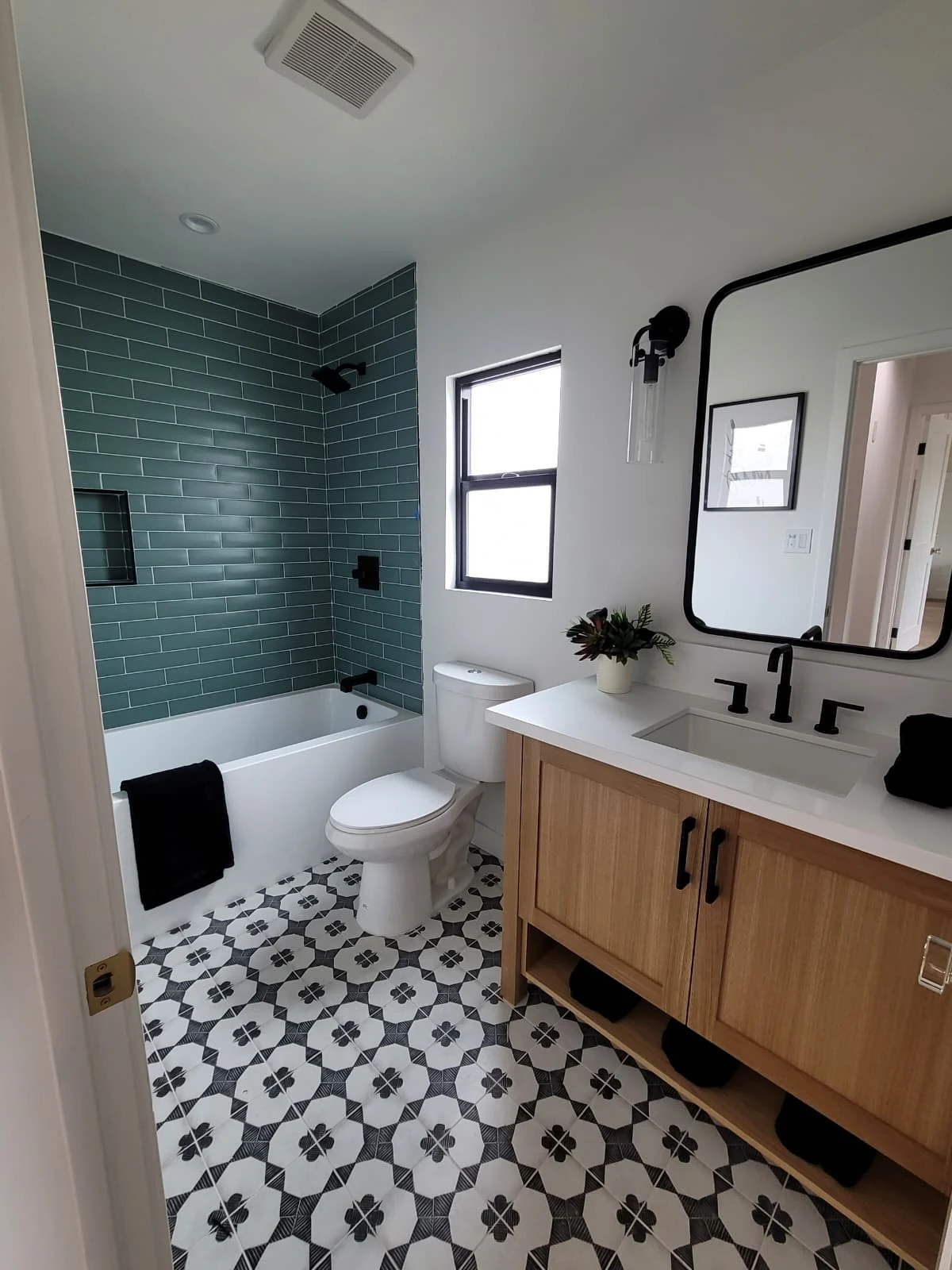 Completed bathroom remodel with teal tile tub surround, custom vanity, and black fixtures
