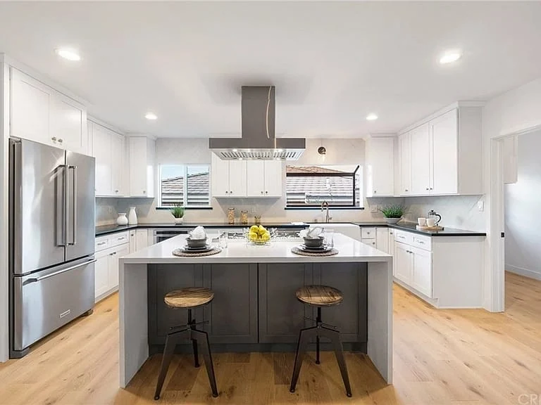 Completed bright kitchen with oversized island, white cabinetry, and wood flooring